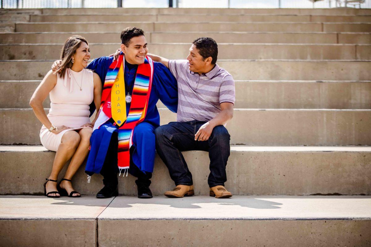 A graduate sitting on a set of stairs with their family