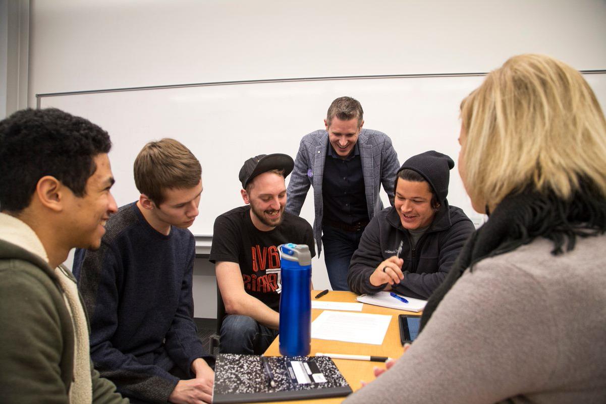 A professor standing up talking to a group of students sitting in a circle
